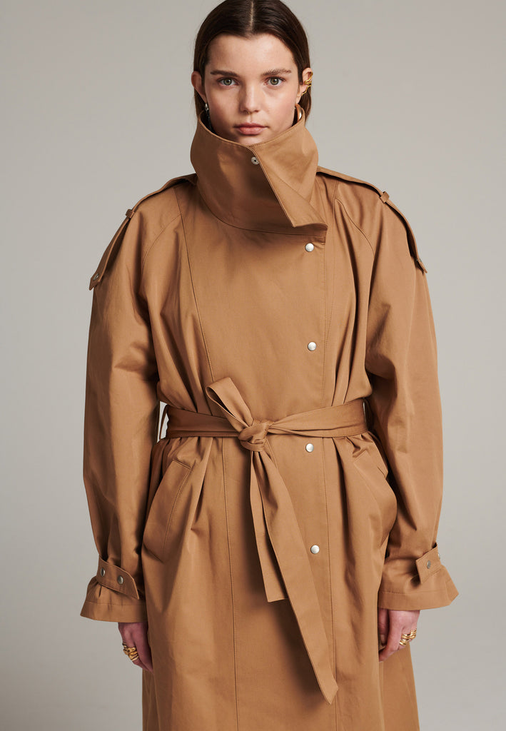 Oversized trench coat tailored from crisp camel cotton for a loose shape. Detailed with silver metal press buttons at front closure at the cuffs. An oversized collar to hide in and a self-fabric belt to cinch the loose oversized fit.