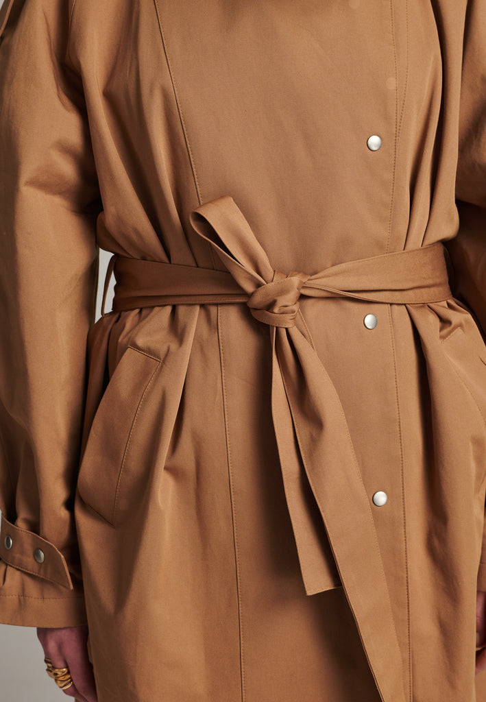 Oversized trench coat tailored from crisp camel cotton for a loose shape. Detailed with silver metal press buttons at front closure at the cuffs. An oversized collar to hide in and a self-fabric belt to cinch the loose oversized fit.