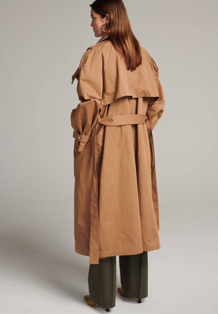 Oversized trench coat tailored from crisp camel cotton for a loose shape. Detailed with silver metal press buttons at front closure at the cuffs. An oversized collar to hide in and a self-fabric belt to cinch the loose oversized fit.