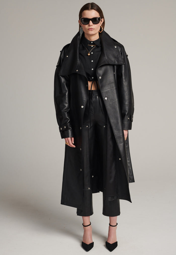 Oversized trench coat crafted in butterly soft lamb leather in black. Detailed with silver metal press buttons at front closure, epaulettes at shoulders and cuffs. Designed with a maxi collar with the snap-fastening buttons and a self-leather belt tp cinch the loose oversized fit.