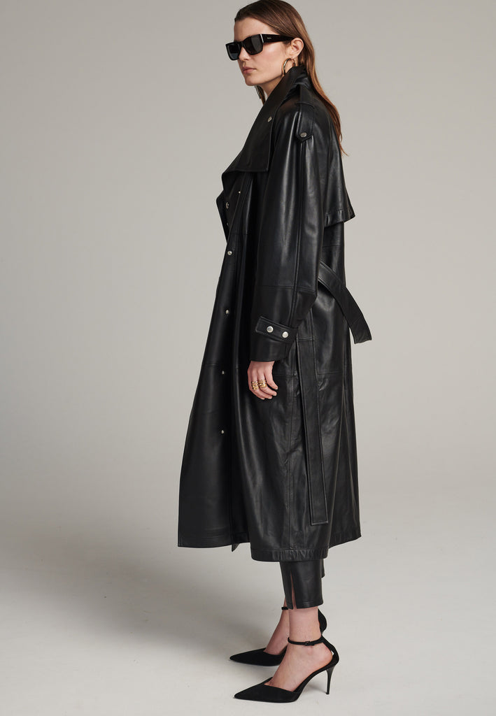 Oversized trench coat crafted in butterly soft lamb leather in black. Detailed with silver metal press buttons at front closure, epaulettes at shoulders and cuffs. Designed with a maxi collar with the snap-fastening buttons and a self-leather belt tp cinch the loose oversized fit.