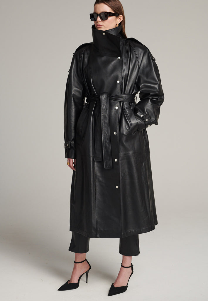 Oversized trench coat crafted in butterly soft lamb leather in black. Detailed with silver metal press buttons at front closure, epaulettes at shoulders and cuffs. Designed with a maxi collar with the snap-fastening buttons and a self-leather belt tp cinch the loose oversized fit.