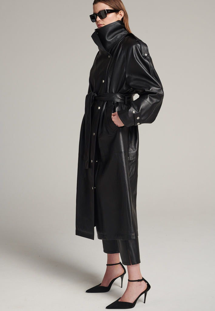 Oversized trench coat crafted in butterly soft lamb leather in black. Detailed with silver metal press buttons at front closure, epaulettes at shoulders and cuffs. Designed with a maxi collar with the snap-fastening buttons and a self-leather belt tp cinch the loose oversized fit.