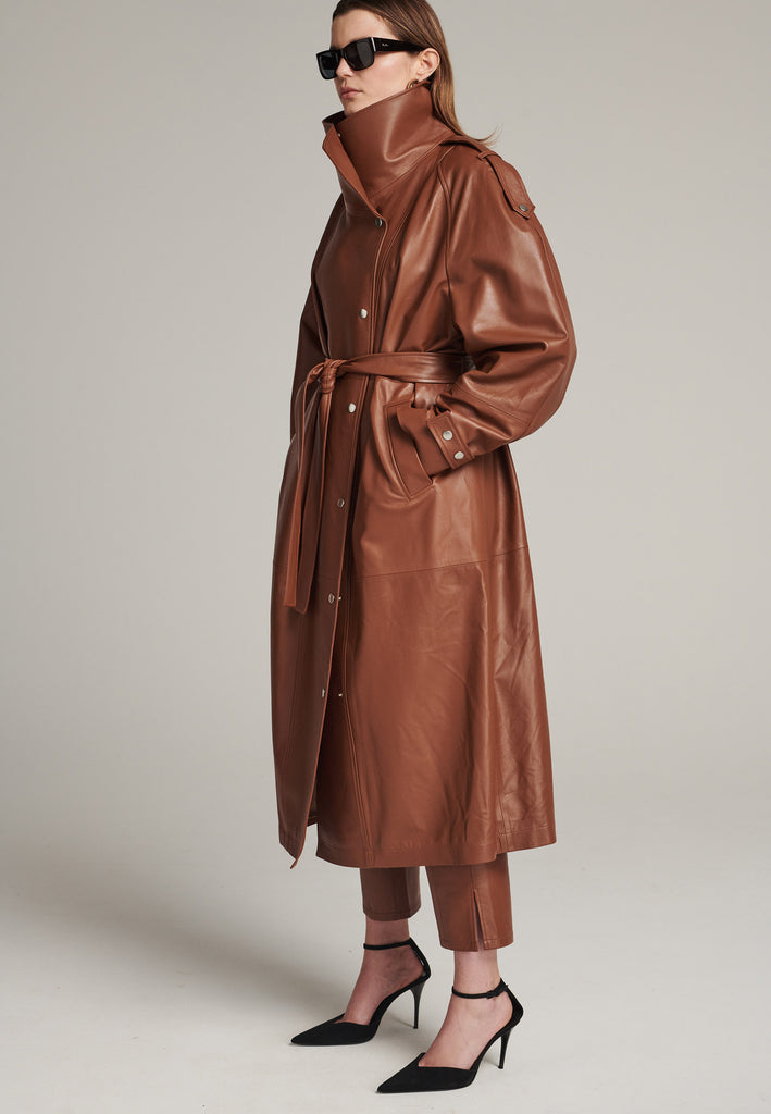 Oversized trench coat crafted in butterly soft lamb leather in cognac. Detailed with silver metal press buttons at front closure, epaulettes at shoulders and cuffs. Designed with a maxi collar with the snap-fastening buttons and a self-leather belt tp cinch the loose oversized fit.