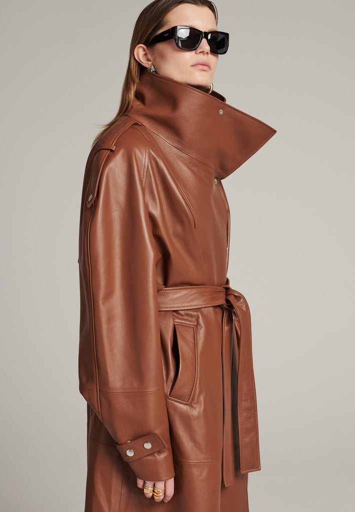 Oversized trench coat crafted in butterly soft lamb leather in cognac. Detailed with silver metal press buttons at front closure, epaulettes at shoulders and cuffs. Designed with a maxi collar with the snap-fastening buttons and a self-leather belt tp cinch the loose oversized fit.