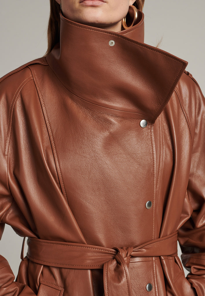 Oversized trench coat crafted in butterly soft lamb leather in cognac. Detailed with silver metal press buttons at front closure, epaulettes at shoulders and cuffs. Designed with a maxi collar with the snap-fastening buttons and a self-leather belt tp cinch the loose oversized fit.