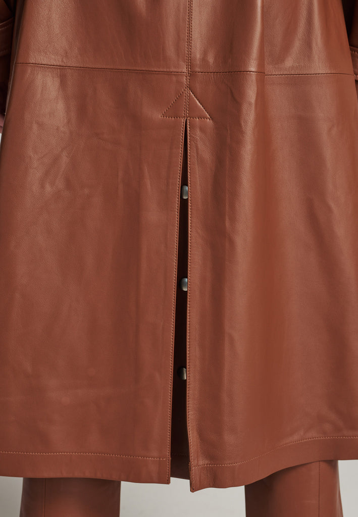 Oversized trench coat crafted in butterly soft lamb leather in cognac. Detailed with silver metal press buttons at front closure, epaulettes at shoulders and cuffs. Designed with a maxi collar with the snap-fastening buttons and a self-leather belt tp cinch the loose oversized fit.