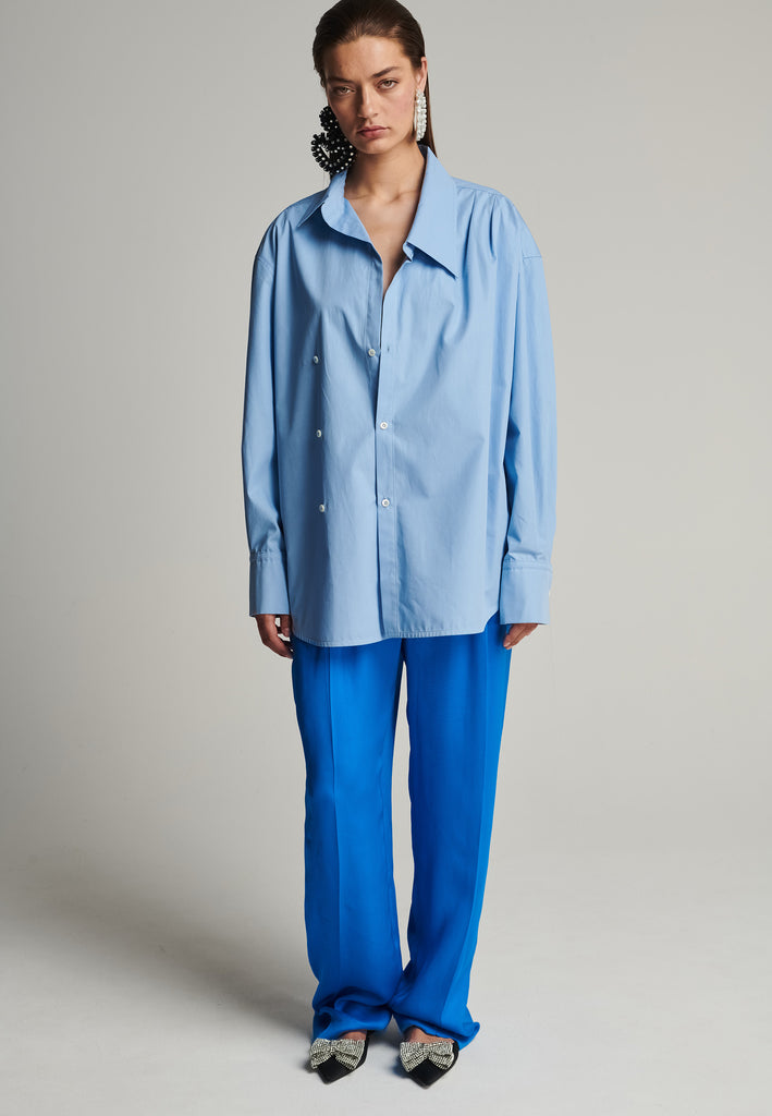 Menswear-inspired wrap-shirt in light blue. Features a second row of buttons, wear it normally or asymmetrically. 2 in 1. Fits oversize.