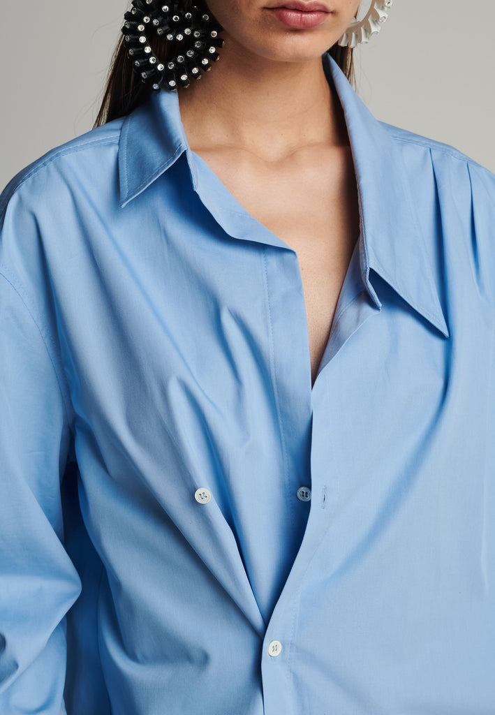 Menswear-inspired wrap-shirt in light blue. Features a second row of buttons, wear it normally or asymmetrically. 2 in 1. Fits oversize.