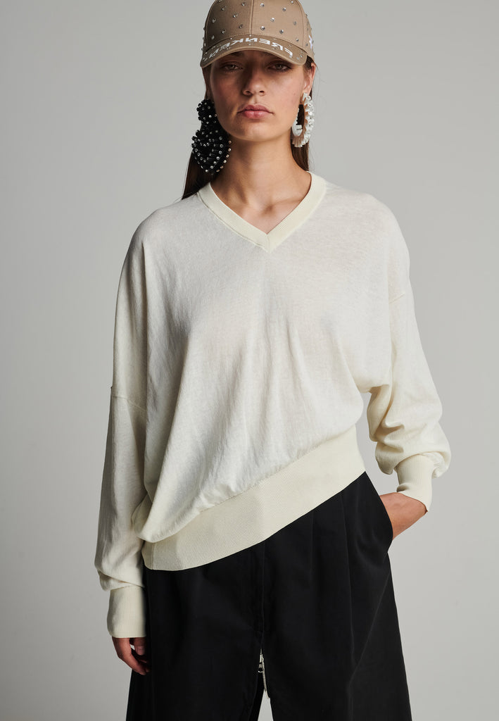 Cotton knitted loose jumper in off-white. Features a v-neck, an asymmetric effect, and wide cuffs. True to size.