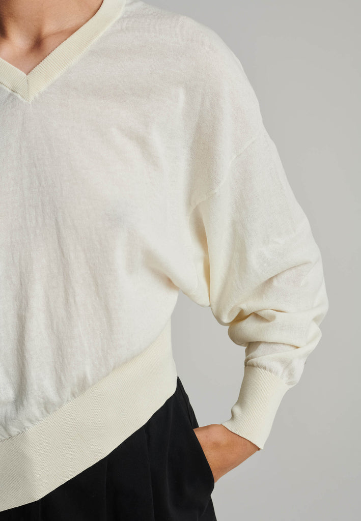 Cotton knitted loose jumper in off-white. Features a v-neck, an asymmetric effect, and wide cuffs. True to size.