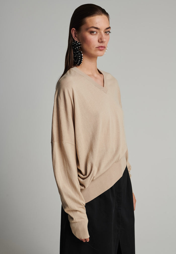 Cotton knitted loose jumper in camel. Features a v-neck, an asymmetric effect, and wide cuffs. True to size.