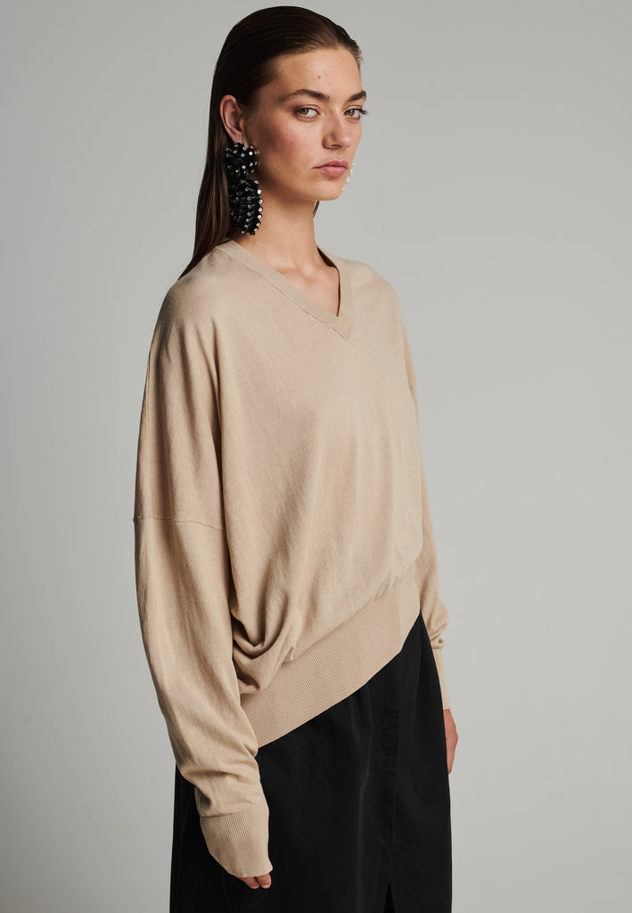 Cotton knitted loose jumper in camel. Features a v-neck, an asymmetric effect, and wide cuffs. True to size.