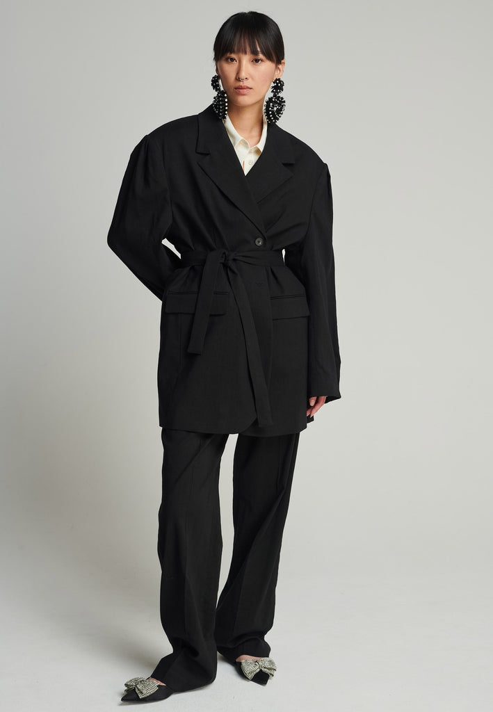 Wide-shouldered blazer in black. Features shoulder-pads, front pockets, and a belt to adjust to your liking. Fits oversize.