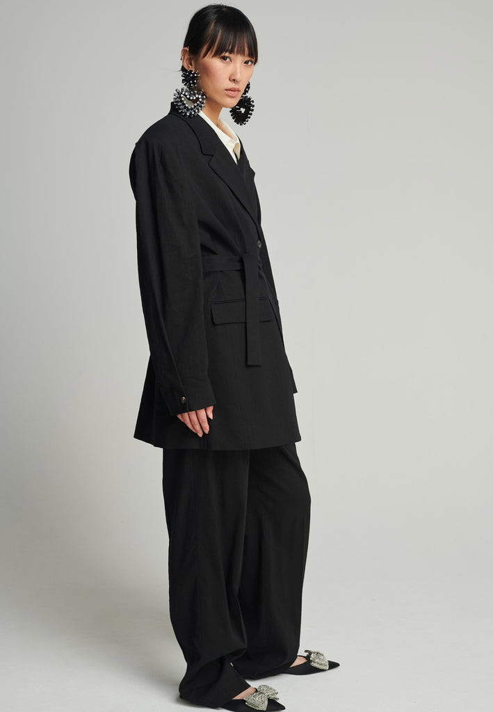 Wide-shouldered blazer in black. Features shoulder-pads, front pockets, and a belt to adjust to your liking. Fits oversize.