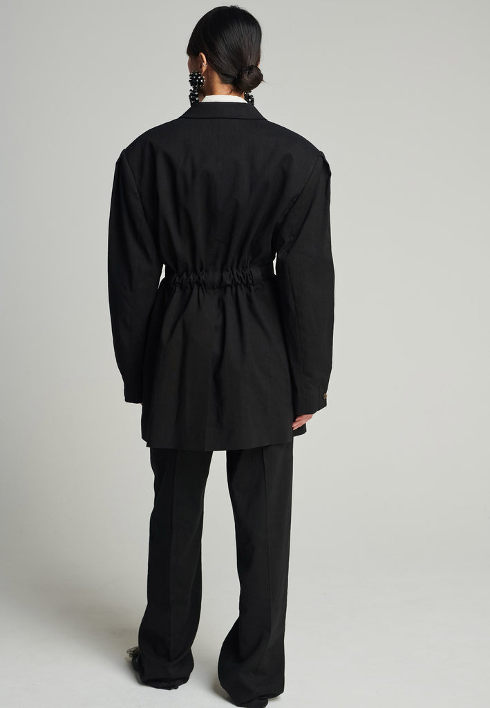 Wide-shouldered blazer in black. Features shoulder-pads, front pockets, and a belt to adjust to your liking. Fits oversize.