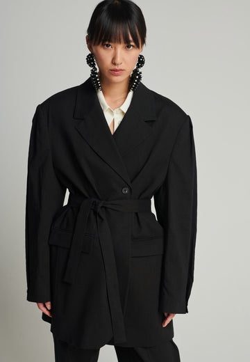 Wide-shouldered blazer in black. Features shoulder-pads, front pockets, and a belt to adjust to your liking. Fits oversize.