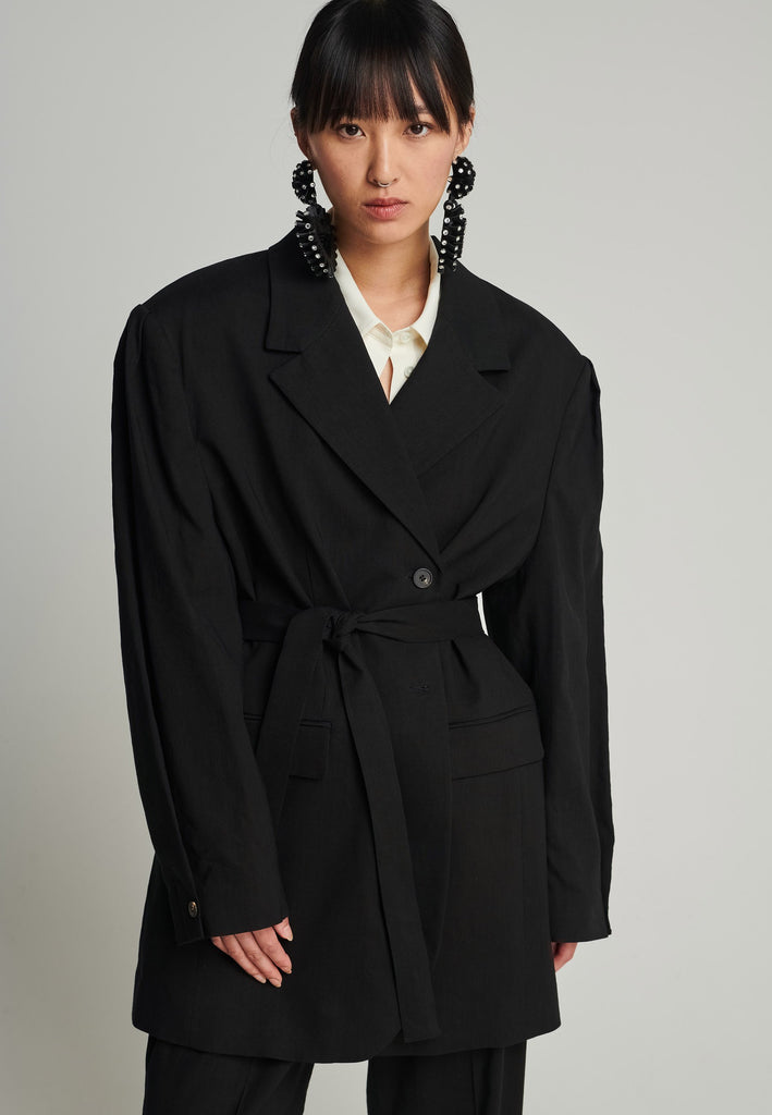 Wide-shouldered blazer in black. Features shoulder-pads, front pockets, and a belt to adjust to your liking. Fits oversize.