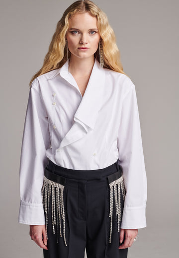 Wide-shouldered asymmetric wrap shirt fitted at the waist. Asymmetric collar structure. Wide relaxed sleeves with multiple buttons on the cuff to adjust the width. Detailed with darts at the waist and six-hole buttons. Cut from crispy cotton poplin.