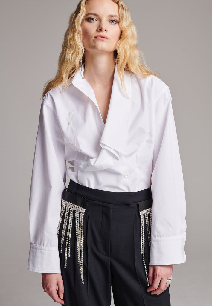 Wide-shouldered asymmetric wrap shirt fitted at the waist. Asymmetric collar structure. Wide relaxed sleeves with multiple buttons on the cuff to adjust the width. Detailed with darts at the waist and six-hole buttons. Cut from crispy cotton poplin.