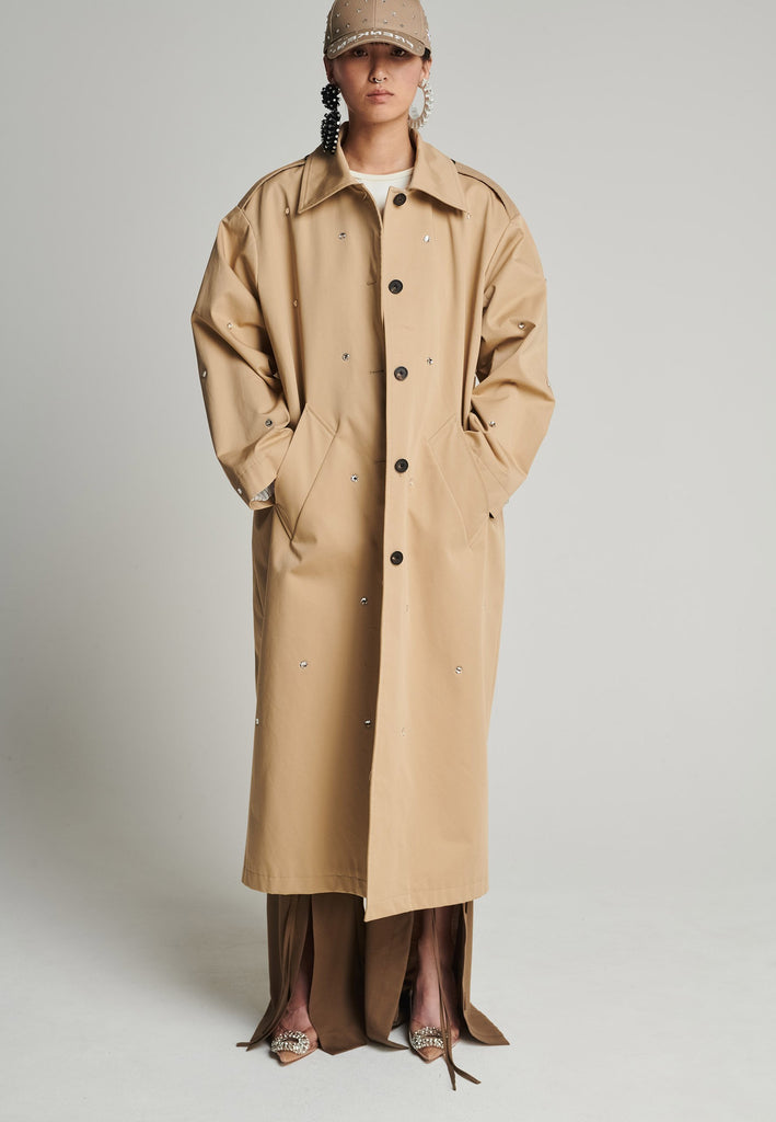 Cotton trenchcoat in camel. Features Swarovski diamonds, pockets, and a single vent. Fits oversize.