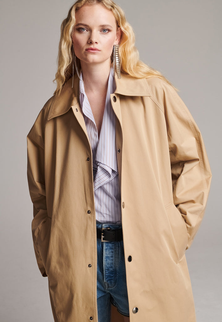 Drawing on the love for classics. Timeless designs like this trench coat are a must-have in the wardrobe. PLEAT is an oversized trench coat tailored from compact cotton twill with metal press stud closure, welt pockets, spread collar and raglan sleeves. Pleat detail showing at the sleeves and side seams.