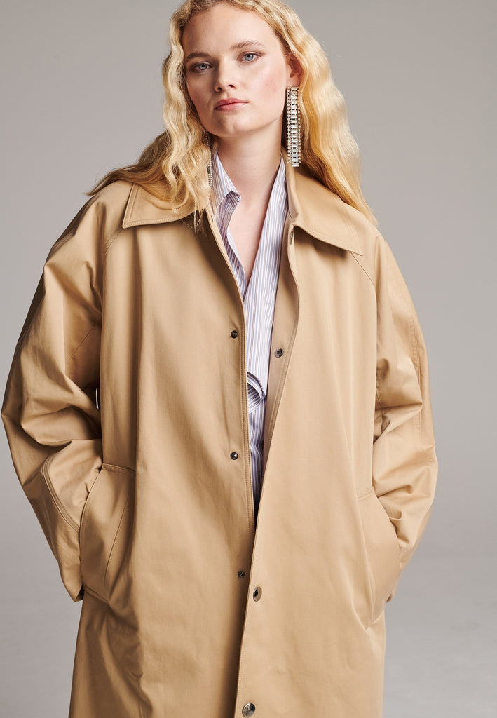 Drawing on the love for classics. Timeless designs like this trench coat are a must-have in the wardrobe. PLEAT is an oversized trench coat tailored from compact cotton twill with metal press stud closure, welt pockets, spread collar and raglan sleeves. Pleat detail showing at the sleeves and side seams.