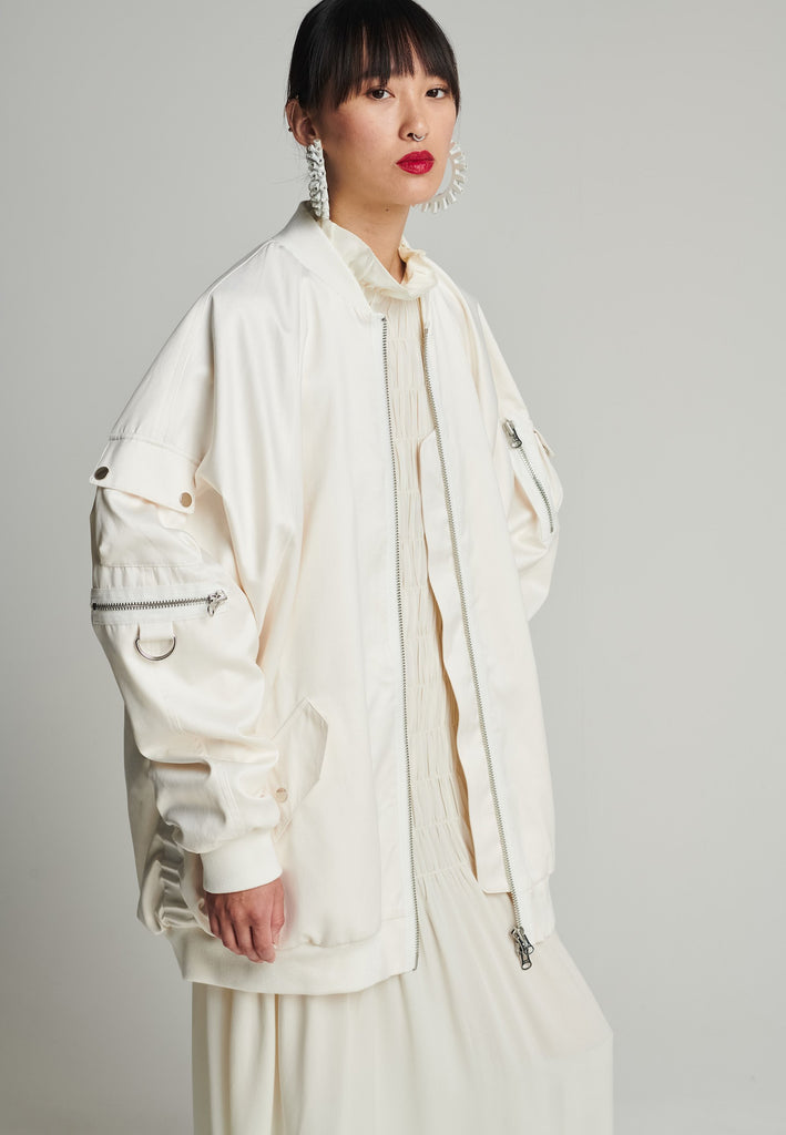 Satin bomber in off-white. Features batwing sleeves, front and arm pockets, zipper closure, and an wrinkled effect on the back. Fits oversize.