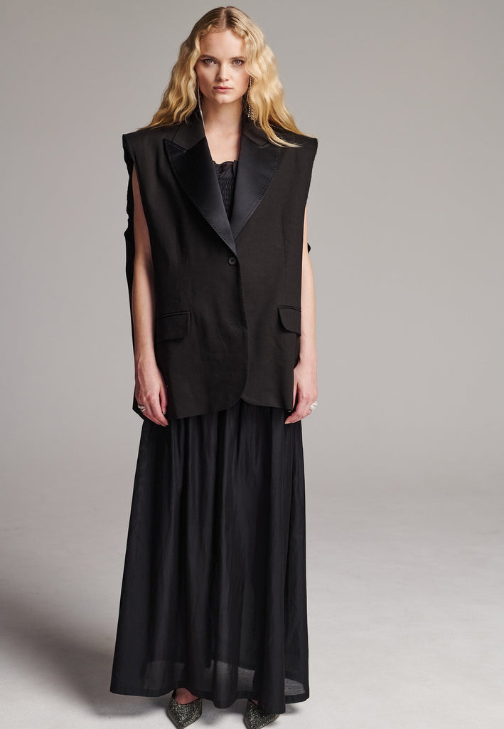 Oversized sleeveless blazer. Padded shoulders, horn button closure, detailed with darts and flap pockets. Raw edge armhole that elevates the piece’s statement. Central back vent, inside welt pocket, tailored with tuxedo satin lapels finished by and needle stitching. Cut from soft summer wool blend and lined with viscose satin.