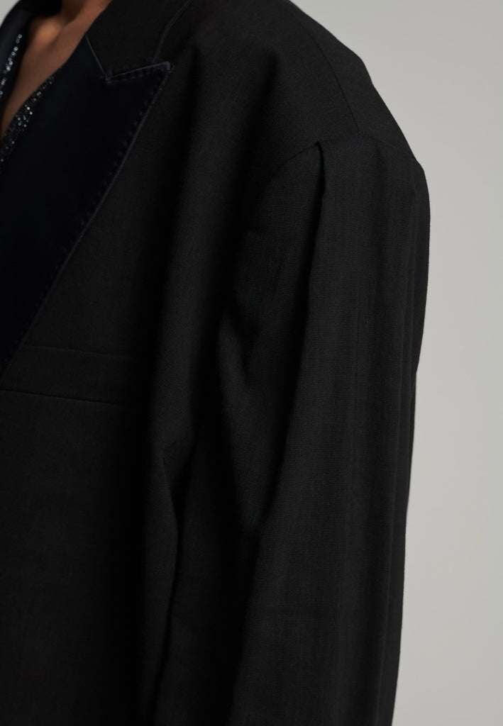 Wide-shouldered short blazer in black. Features shoulder-pads, pockets, and exaggerated long sleeves. Fits oversize