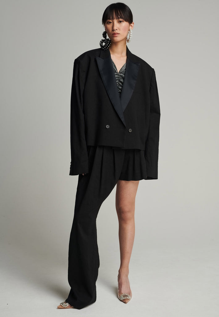 Wide-shouldered short blazer in black. Features shoulder-pads, pockets, and exaggerated long sleeves. Fits oversize
